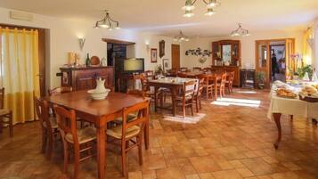 A spacious dining area with wooden tables and chairs, a television, and a kitchen area in the background.