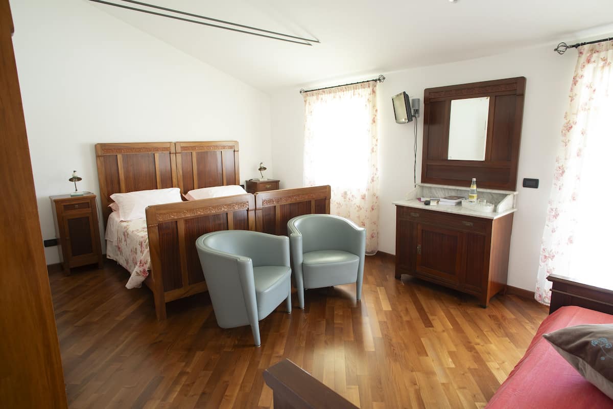 A bedroom with a wooden bed, two chairs, a nightstand, a dresser, and a mirror.