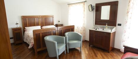 A bedroom with a wooden bed, two chairs, a nightstand, a dresser, and a mirror.