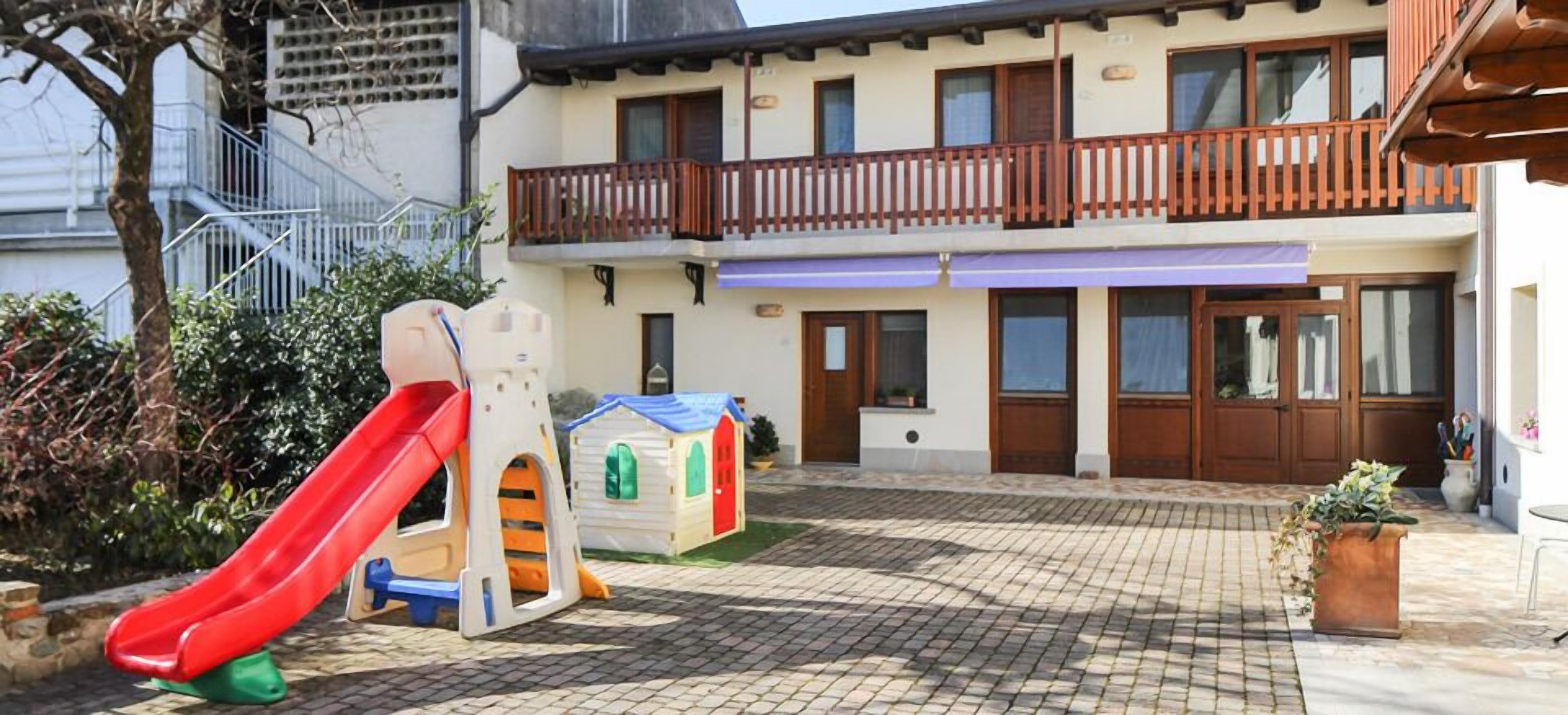 Une cour comprenant un espace de jeux pour enfants, avec notamment un toboggan et une petite maison de jeux.