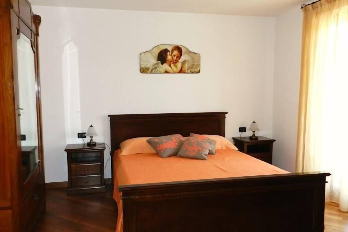 A bedroom with a wooden bed, two bedside tables, a nightstand, a mirror, and a painting on the wall.