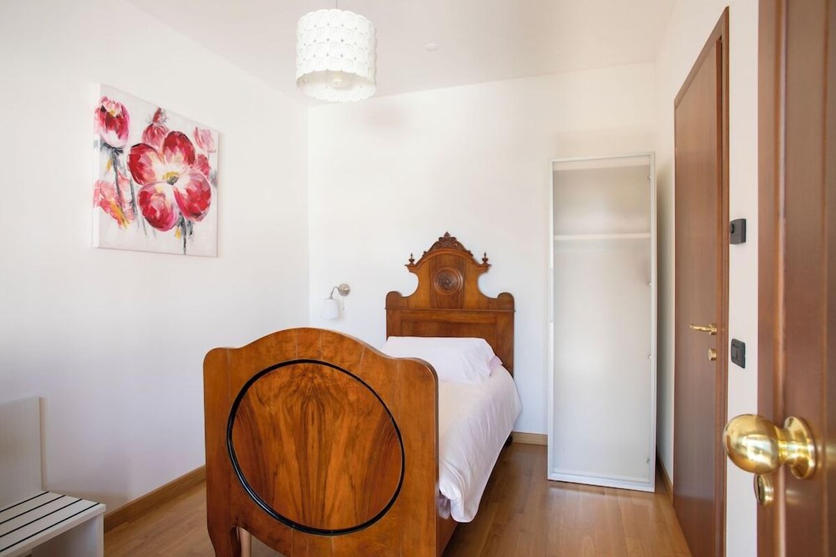 Een slaapkamer met een houten bed, een witte muur, een bloemen schilderij en een deur.
