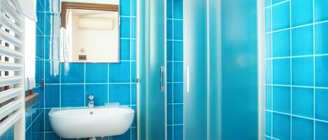A bathroom with blue tiles, a white sink, a bidet, and a glass shower enclosure.