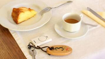 Un plato con una porción de pastel, una taza de café y un llavero con un dije sobre una mesa.