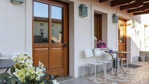 Un bâtiment doté d’une porte en bois, de murs blancs et d’un patio carrelé avec des sièges d’extérieur.