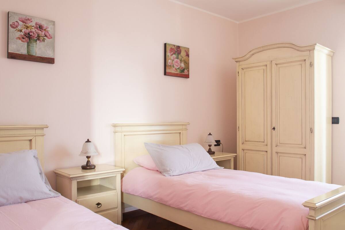 A bedroom with two beds, wooden headboards, a wardrobe, and a nightstand with a lamp.