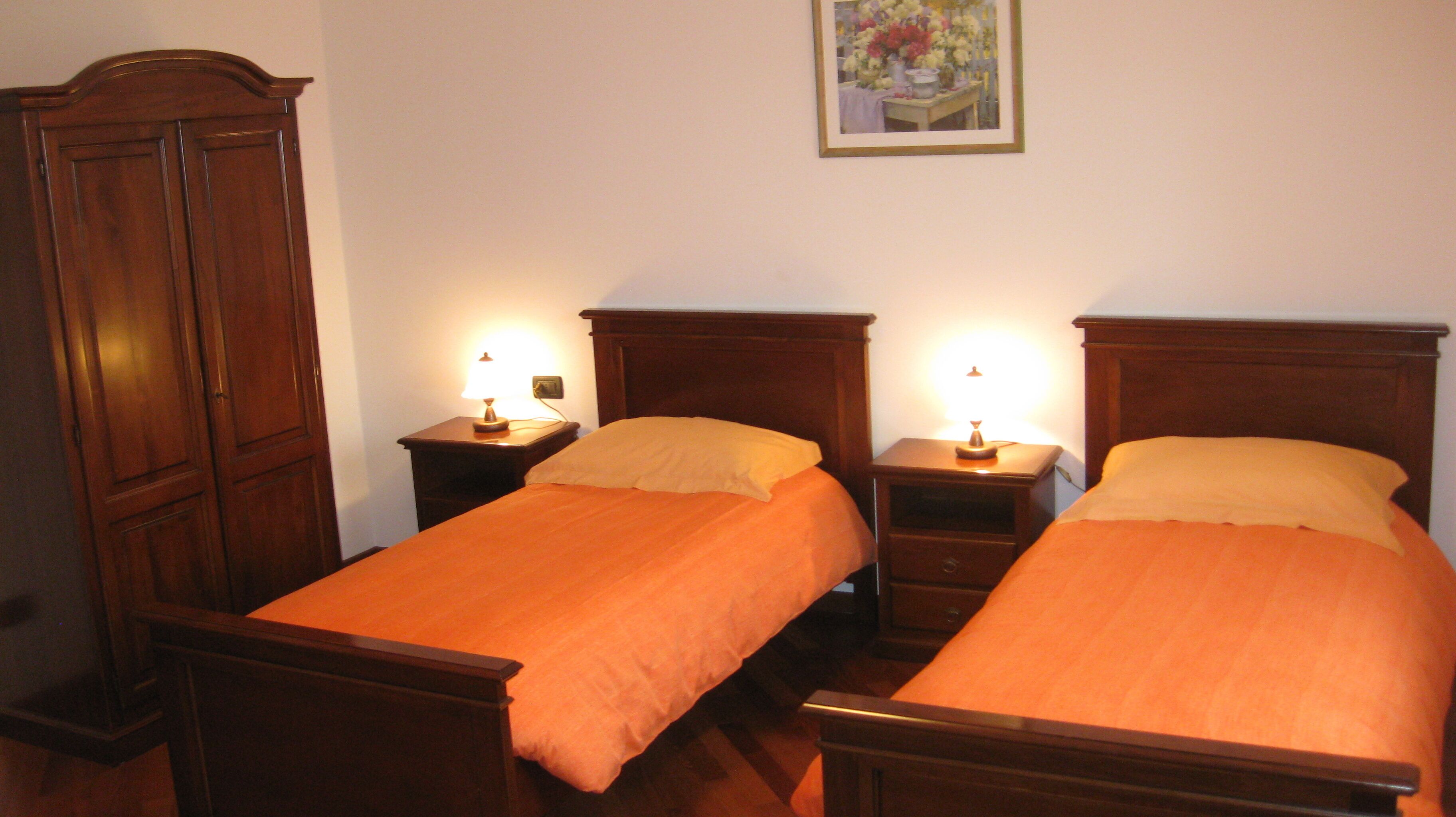 Una habitación con dos camas individuales, cabeceros de madera, mesitas de noche con lámparas y un armario de madera.