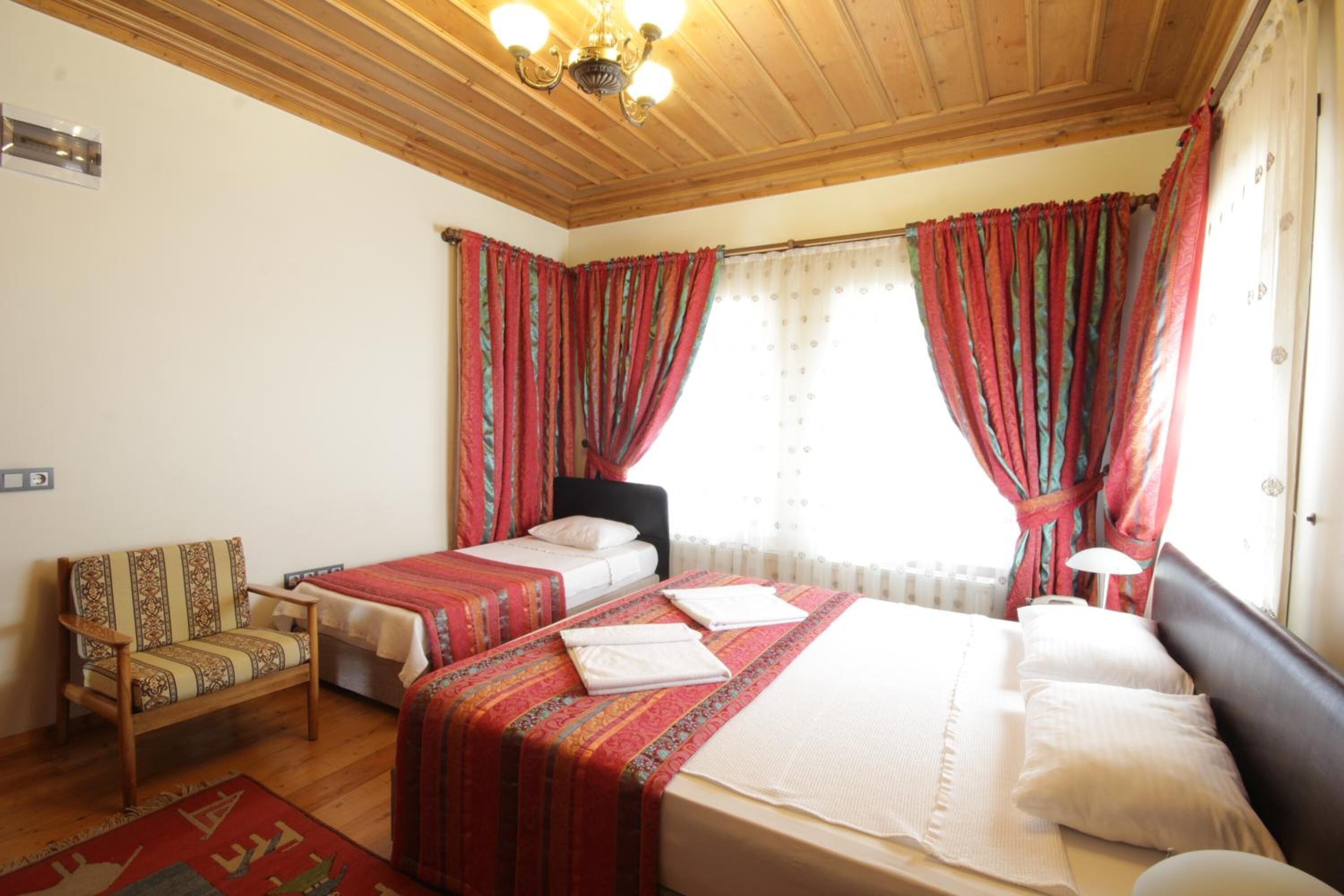 A bedroom with two beds, a chair, and a window with curtains.