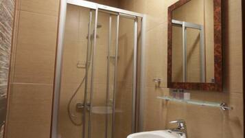 A bathroom with a glass shower enclosure, a white sink, and a mirror with a decorative frame.