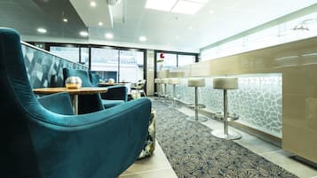 Un hall d’hôtel moderne avec des fauteuils de couleur turquoise, une moquette à motifs et une cloison en verre au motif rappelant la pierre.