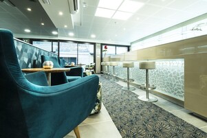 Un moderno vestíbulo de hotel con sillas color turquesa, alfombra estampada y un panel de vidrio con diseño que imita la piedra.