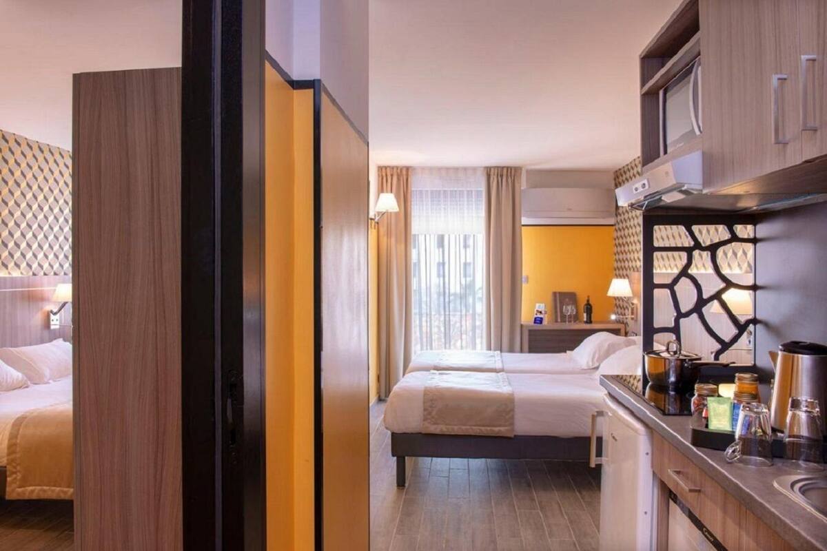 A hotel room with two beds, a kitchenette, and a bathroom.
