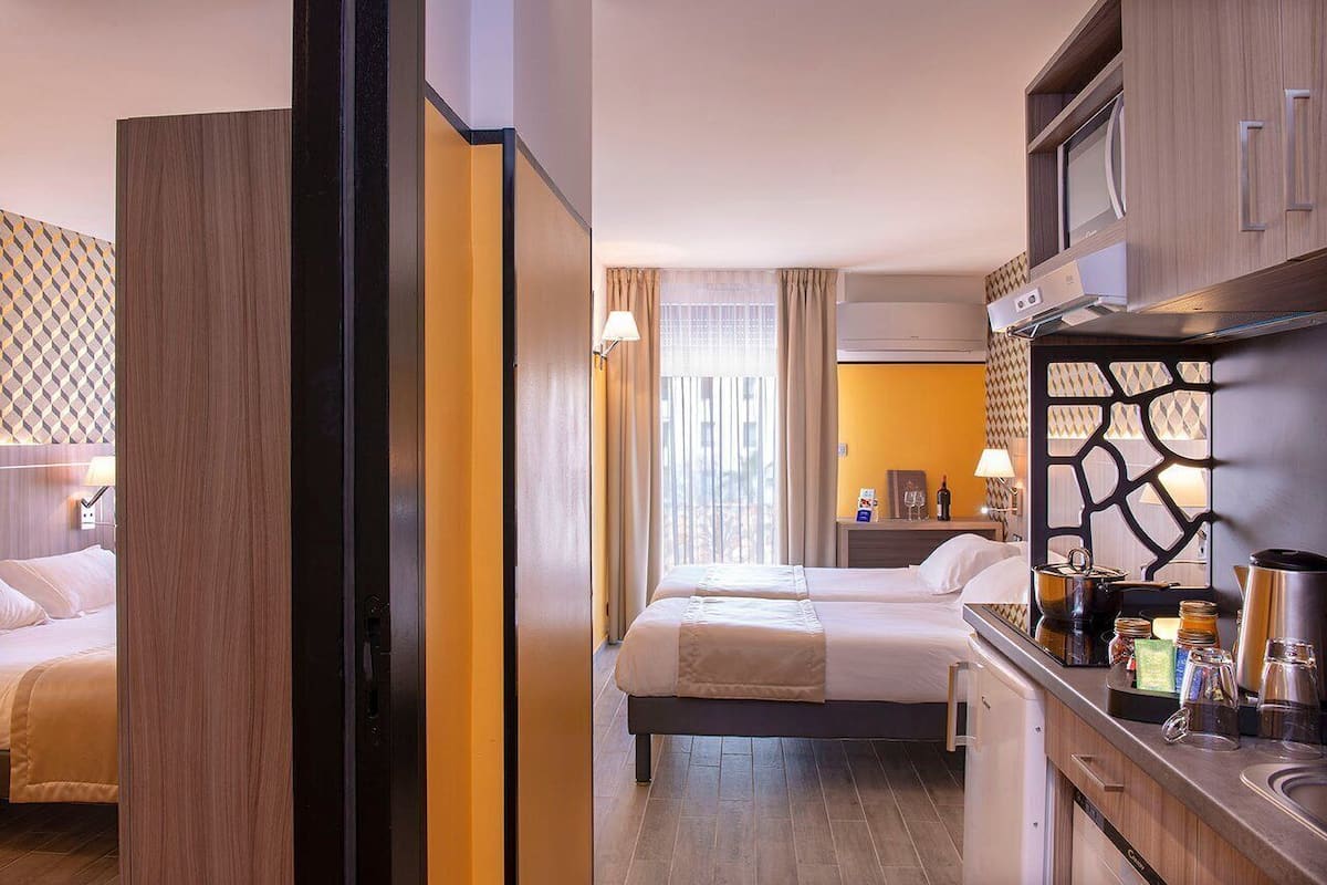 A hotel room with two beds, a kitchenette, and a bathroom.