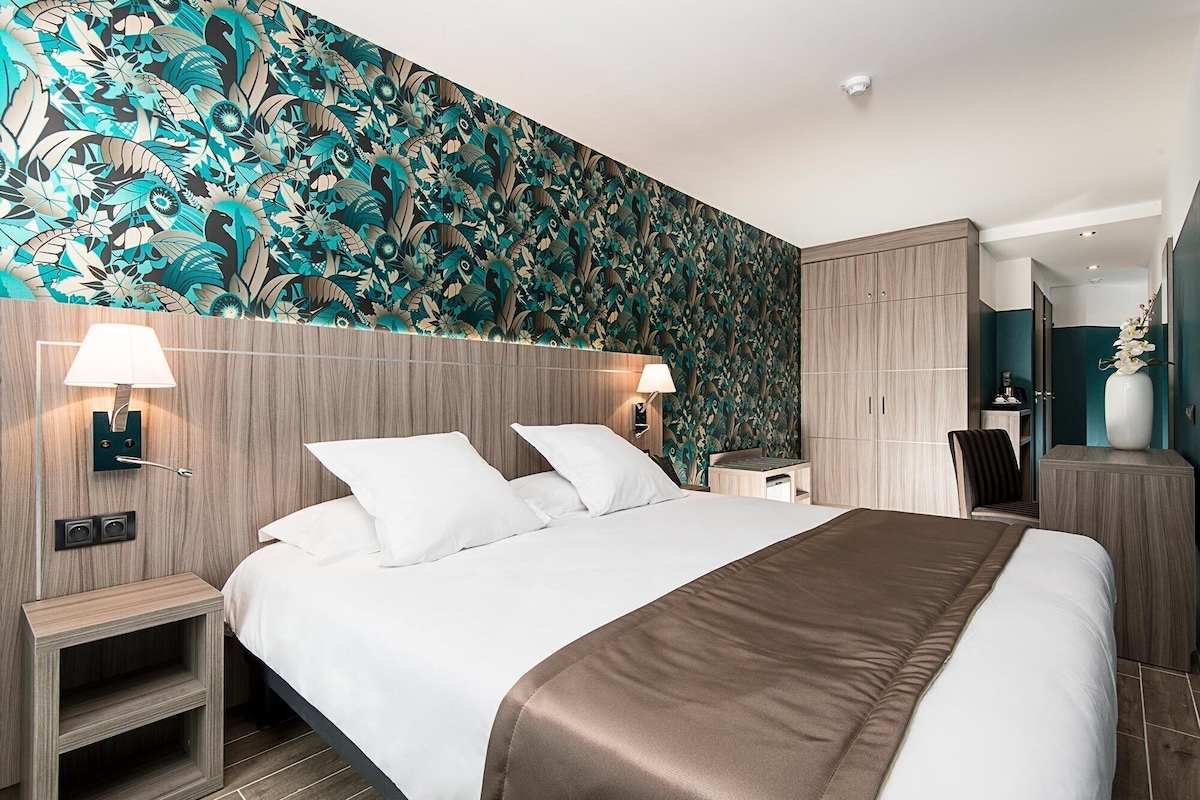 A modern hotel room with a large bed, two bedside tables, a wardrobe, and a floral wallpaper.
