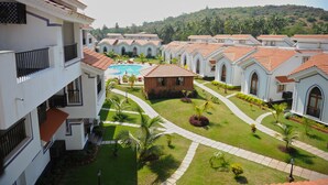 A hotel courtyard with a swimming pool, multiple buildings with red-tiled roofs, and a hilly landscape in the background. - Riviera Hermitage (Arpora)
