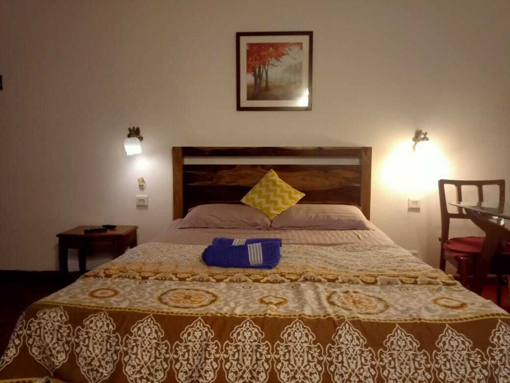 Habitación de hotel con una cama grande, cabecera de madera, un cuadro en la pared y dos lámparas de noche.