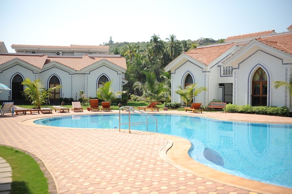 A swimming pool with lounge chairs and a tiled deck.