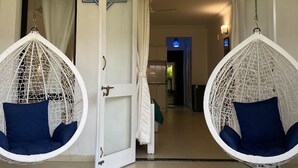 A room with two white hanging chairs with blue cushions, a white door, and a ceiling fan. - Riviera Hermitage (Arpora)