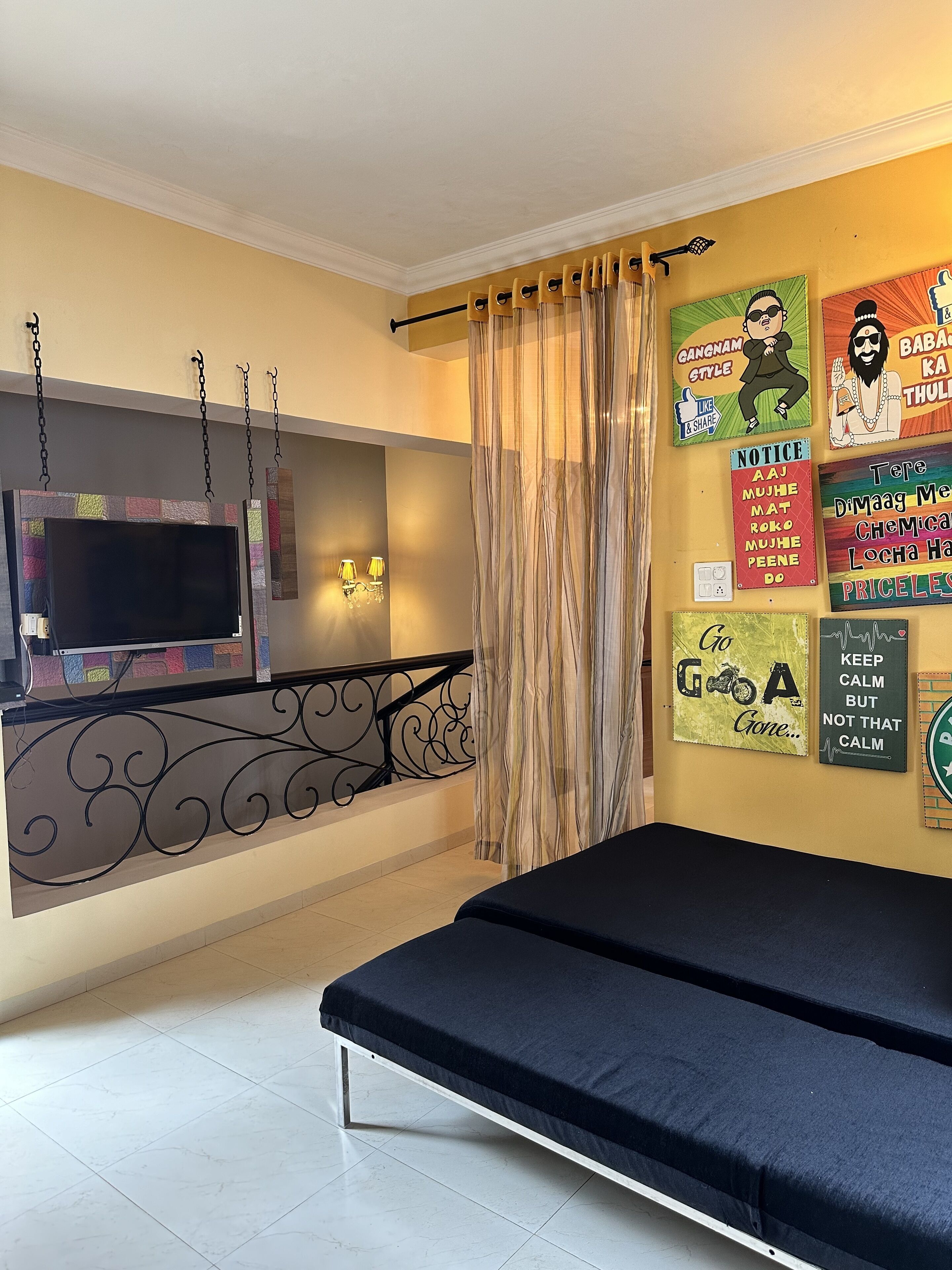 Una habitación con una cama, un televisor montado en la pared y varios carteles decorando la pared.