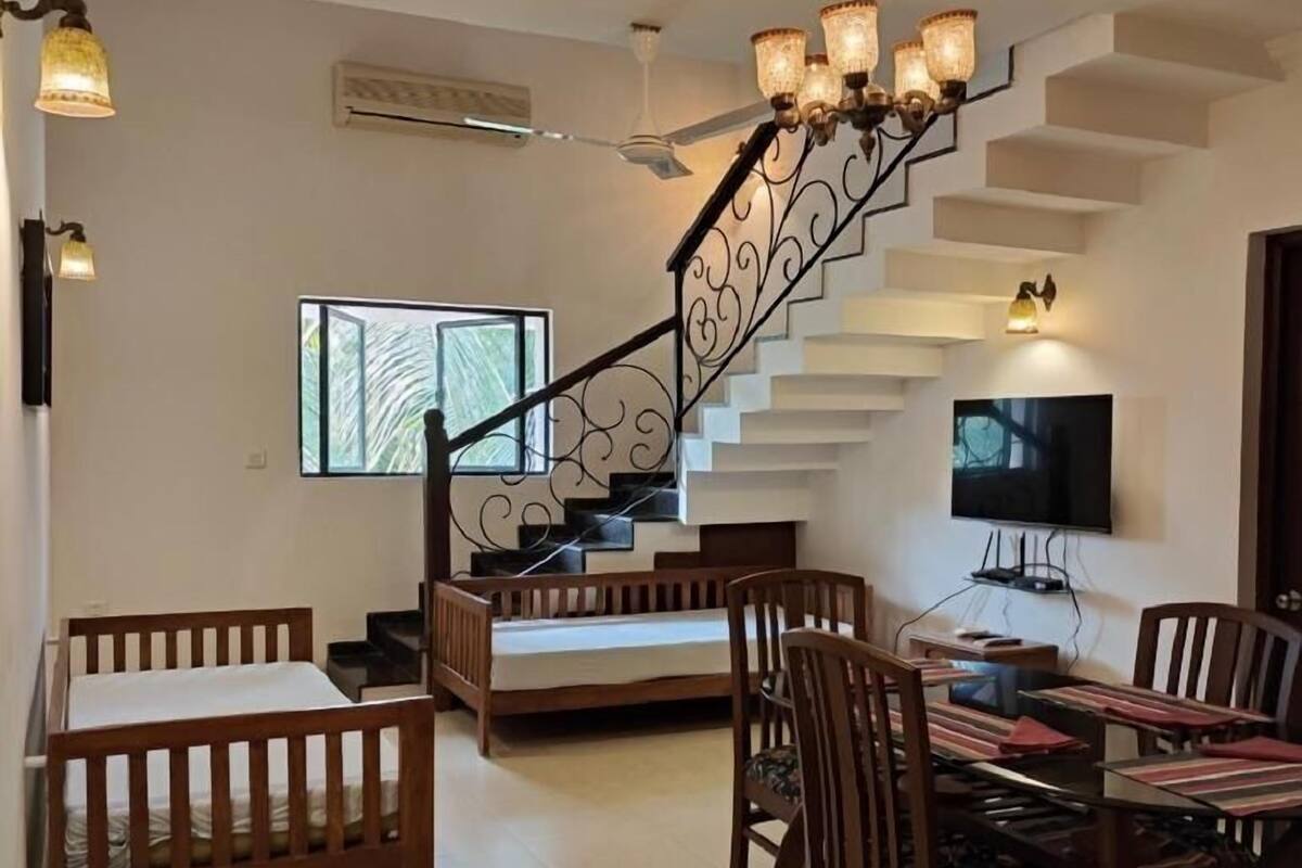 Una sala de estar moderna con una escalera, un comedor con muebles de madera y un televisor de pantalla plana montado en la pared.