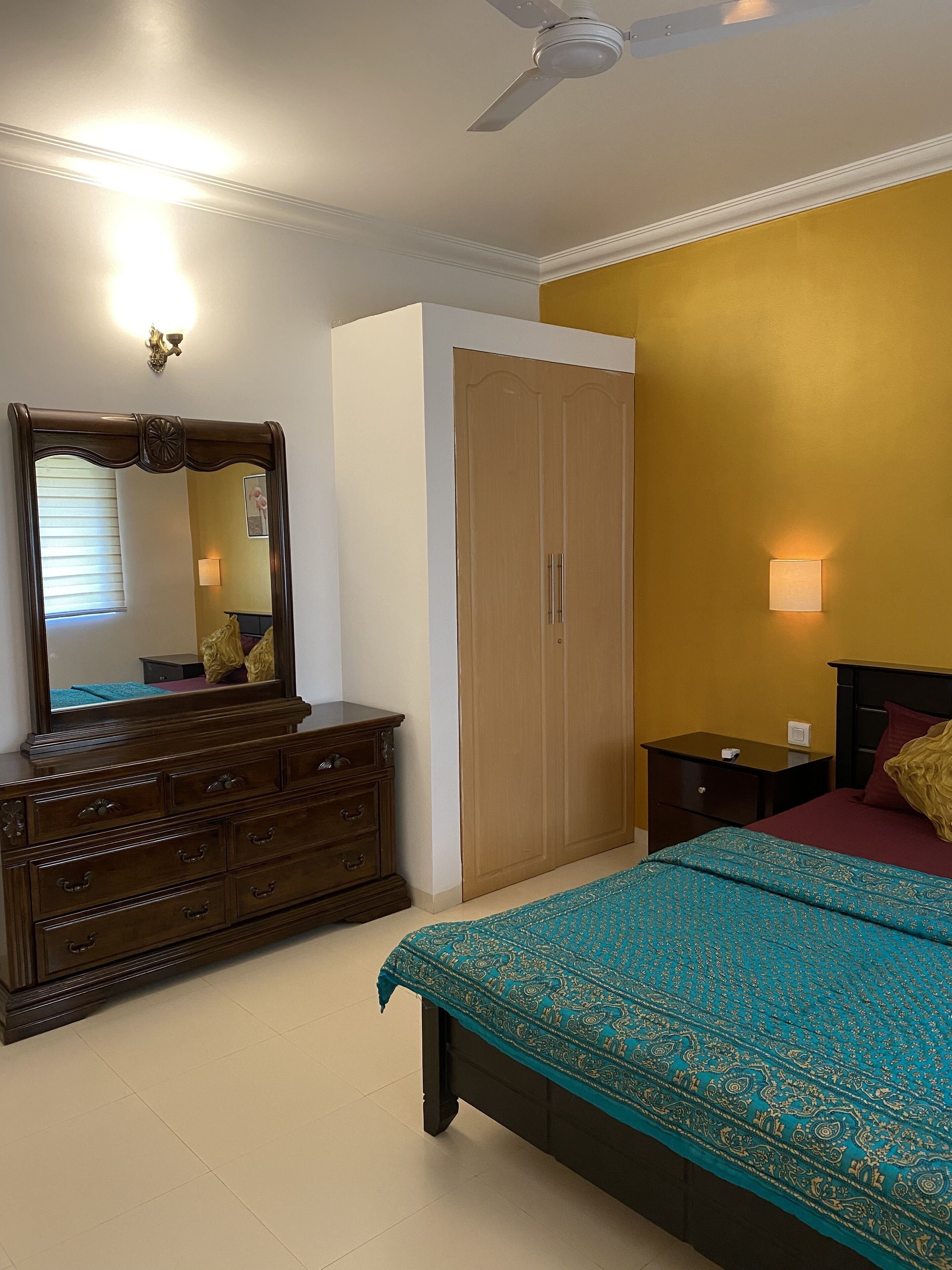 Un dormitorio con cama, cómoda, armario, mesita de noche, lámpara y ventilador de techo.