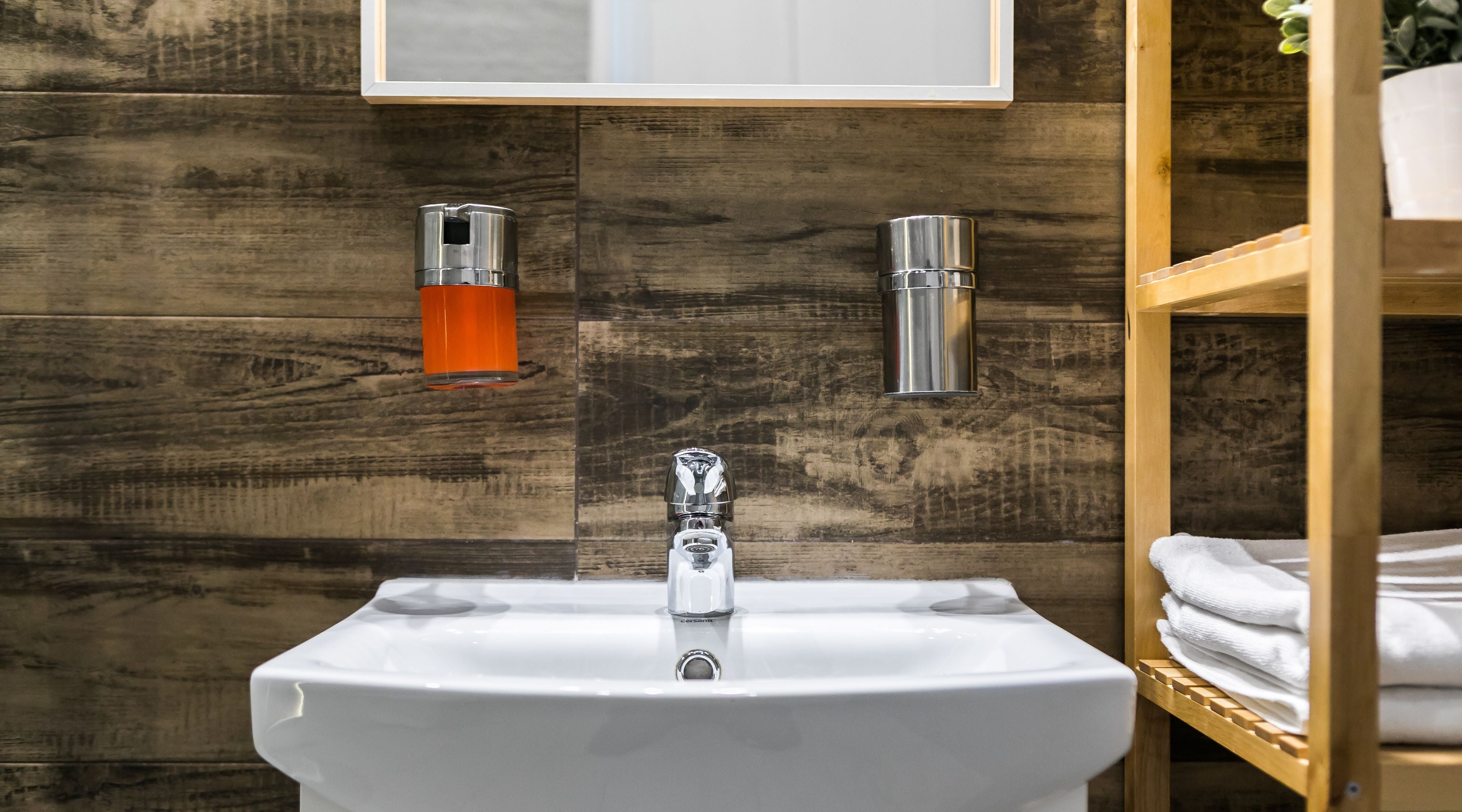 Une salle de bain avec un lavabo blanc, un lambris en bois et une étagère en bois où sont pliées des serviettes.