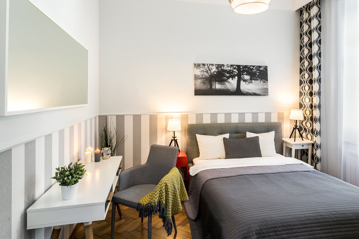 A hotel room with a bed, bedside tables, a chair, a desk, and a potted plant.