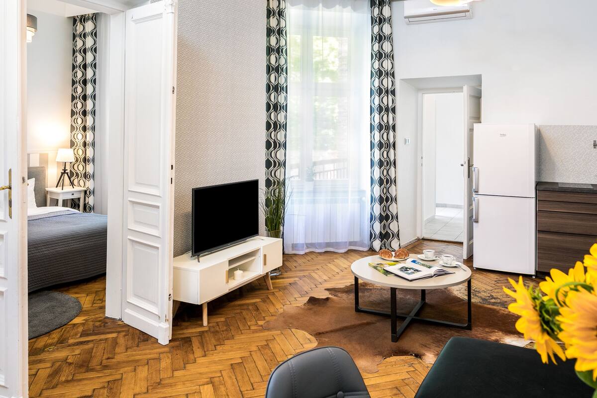 Un salon moderne doté d’un téléviseur à écran plat, d’un canapé, d’une table basse et d’un coin repas avec un réfrigérateur.