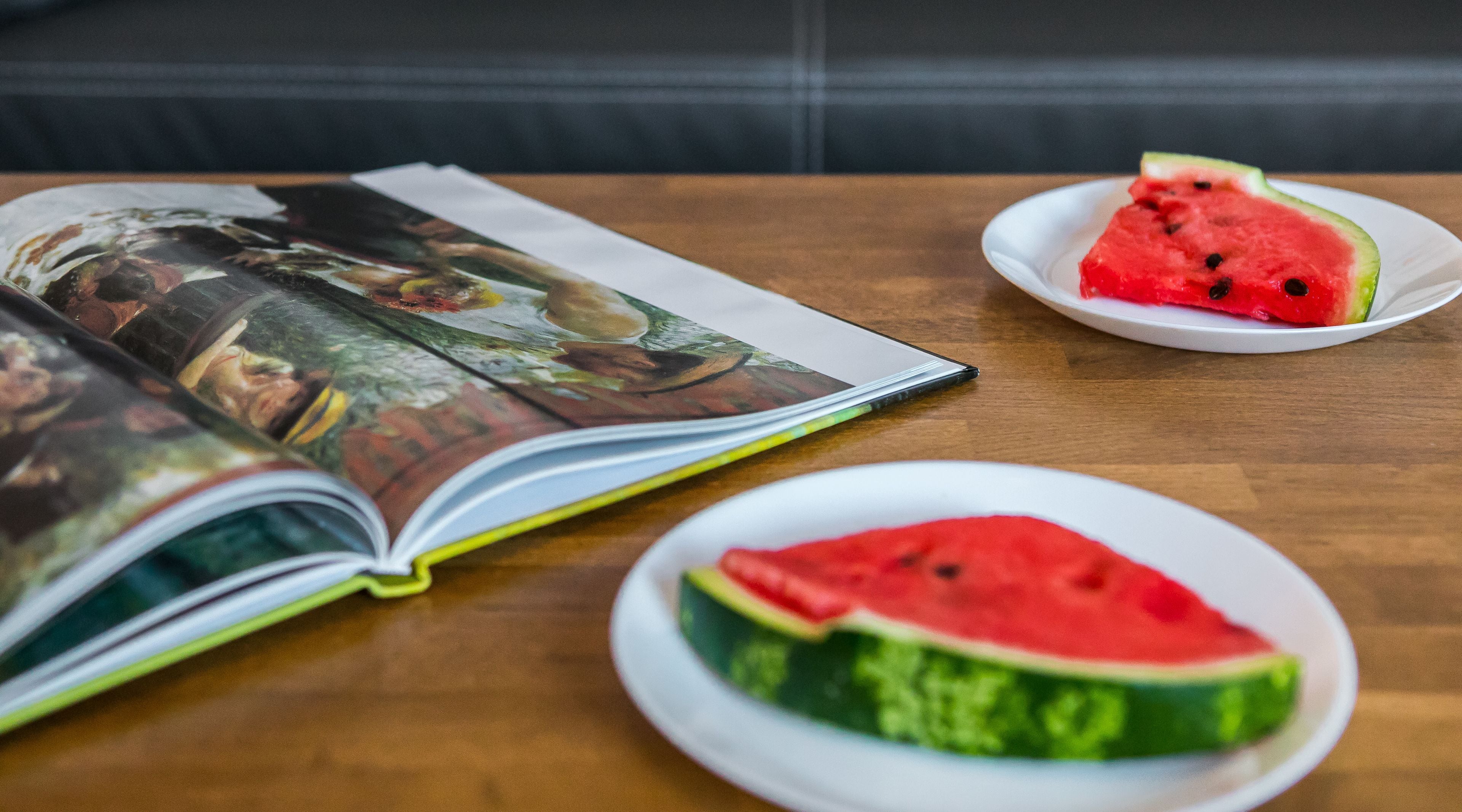 An open book on a wooden table with two plates of watermelon slices.