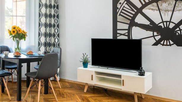 A dining area with a round table, four chairs, a vase with sunflowers, and a TV on a white cabinet. - Old Town Residence BIS (Kraków)