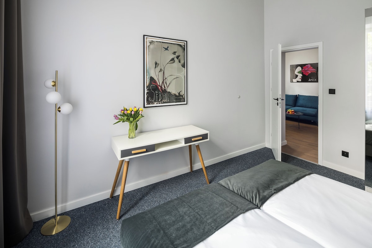 Un dormitorio moderno con una cama, mesitas de noche, un escritorio y una lámpara de pie.