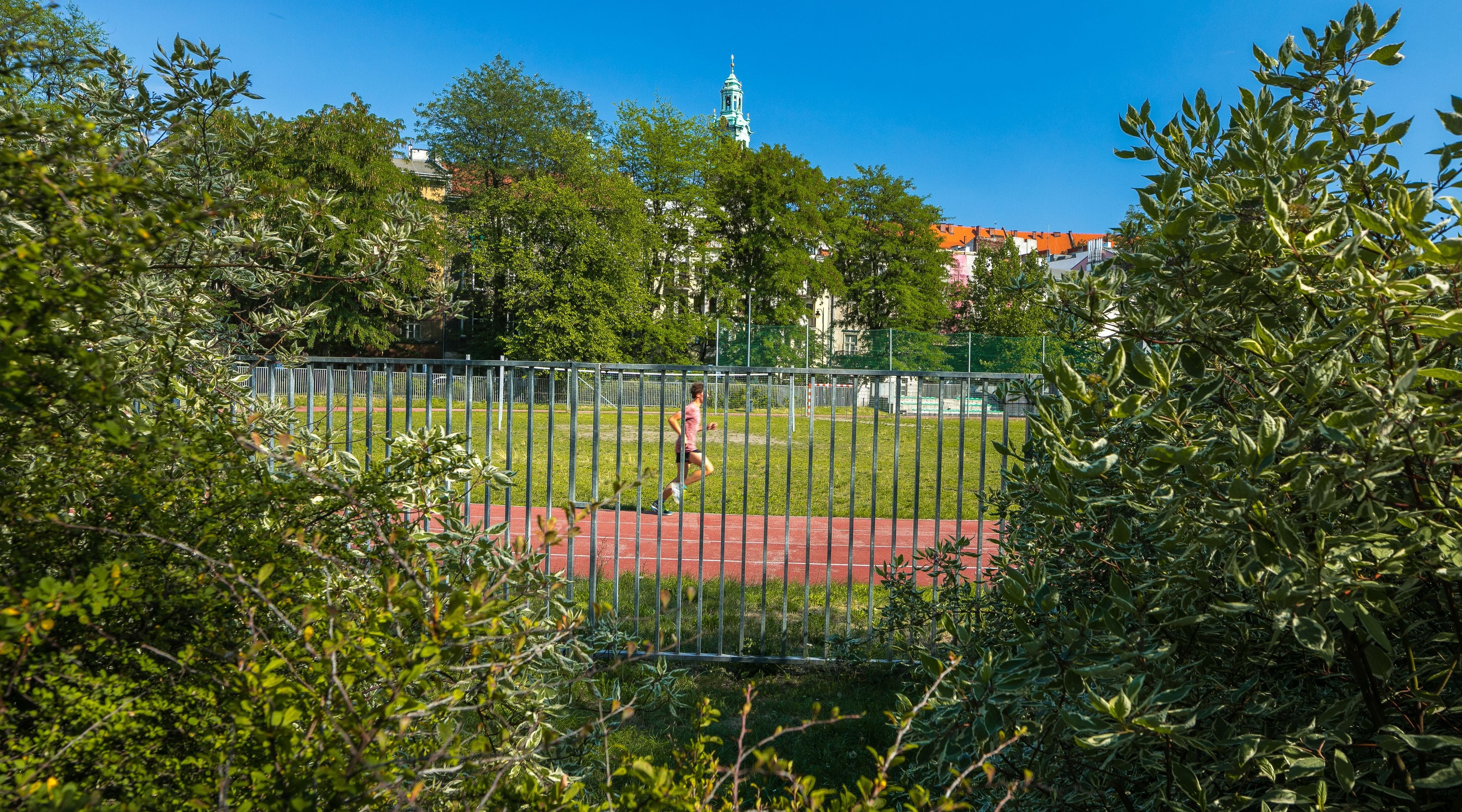 A park with a running track, surrounded by trees and a fence.