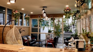 A cozy indoor seating area with wicker chairs, a wooden table, and hanging plants. - I Talay Lodge Boutique Hotel (Rayong)