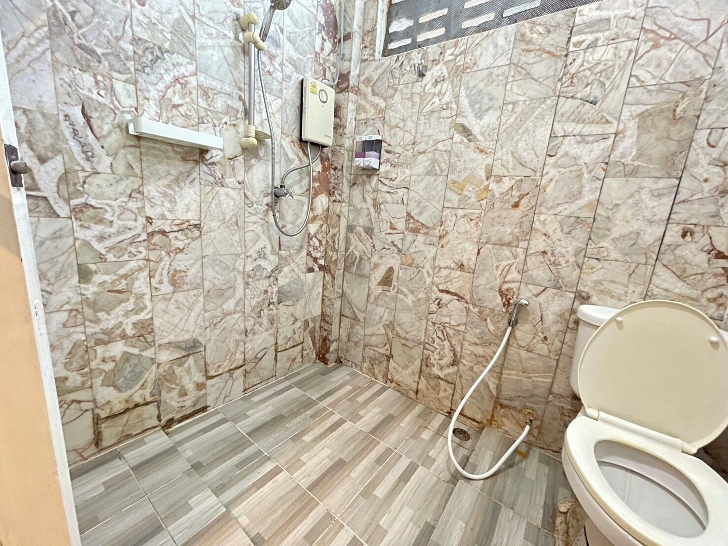 Un baño con paredes de mármol, inodoro y zona de ducha.