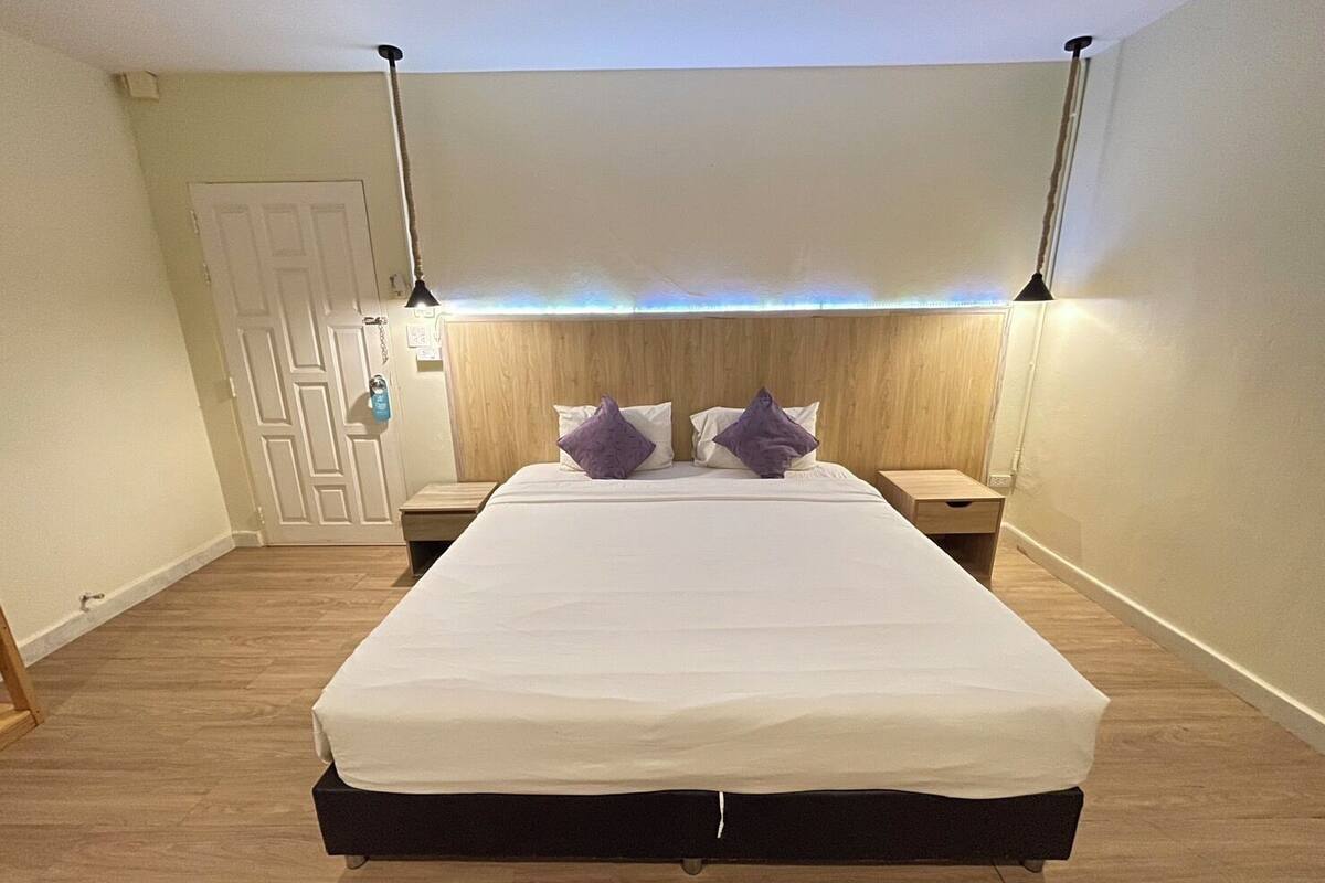 Une chambre à coucher avec un grand lit, une tête de lit en bois, deux tables de chevet et une porte.