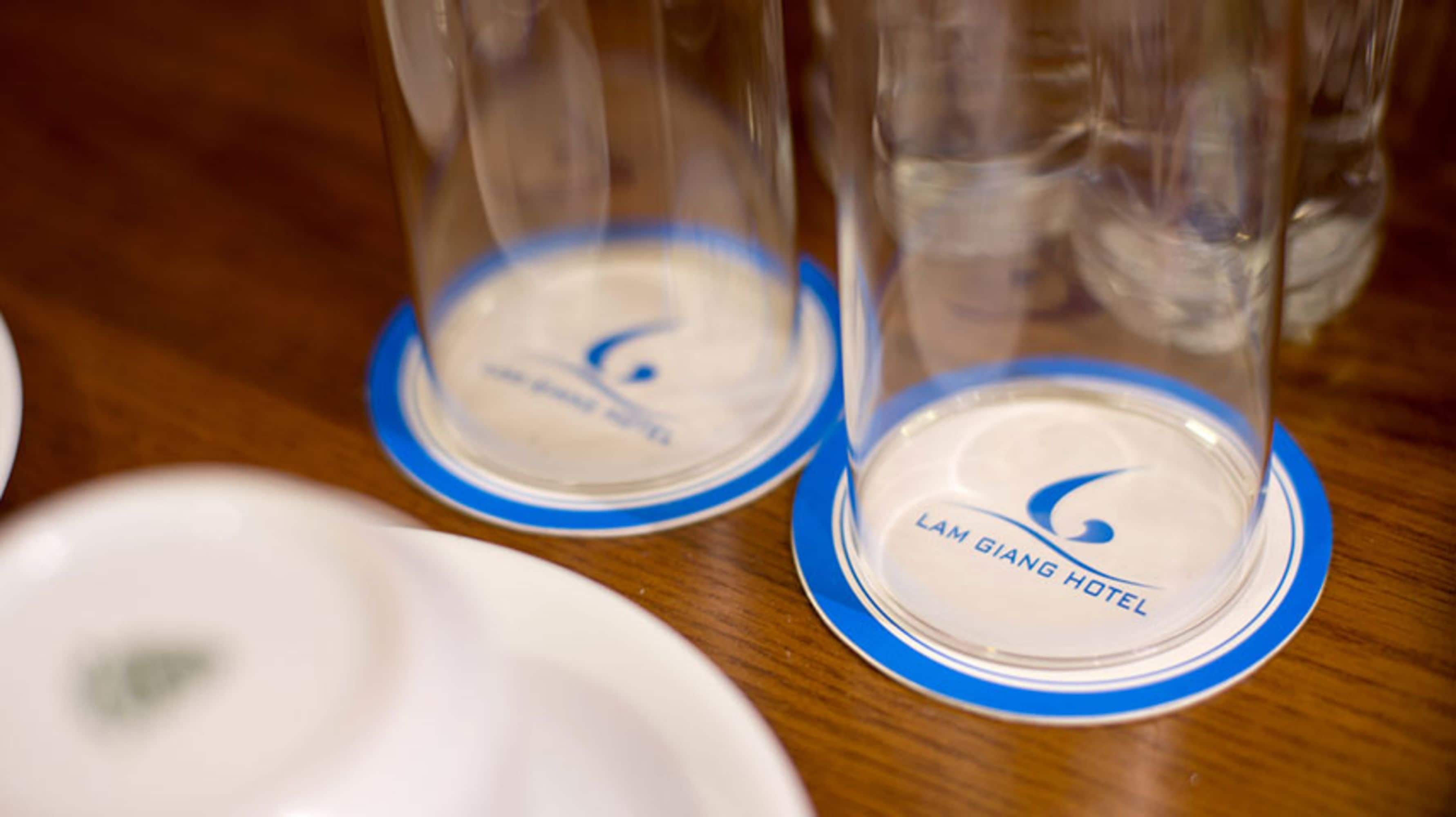 A close-up of a table with clear glass tumblers on blue-rimmed white plates, each labeled with "LAM GIANG HOTEL".