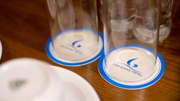 A close-up of a table with clear glass tumblers on blue-rimmed white plates, each labeled with "LAM GIANG HOTEL".
