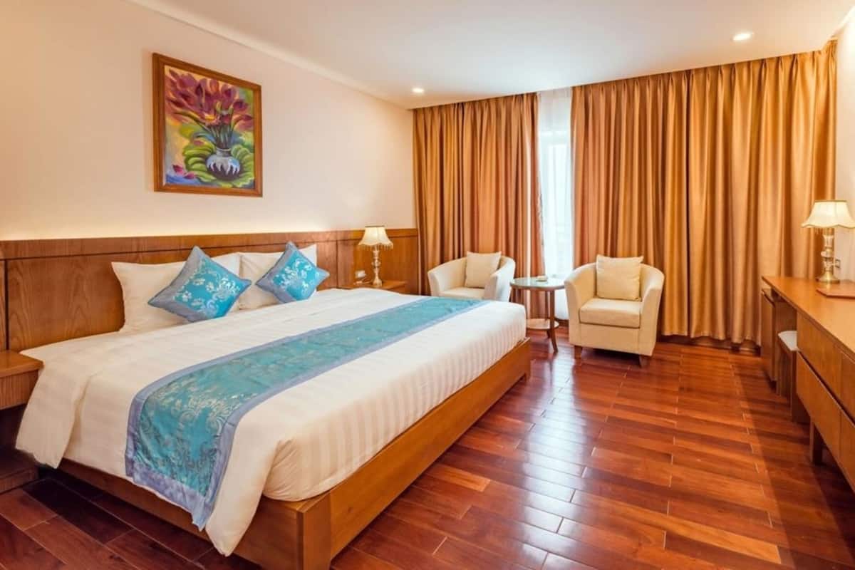 A hotel room with a large bed, a desk, a chair, and a small table.