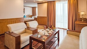 A hotel room with a wooden floor, a sofa, a coffee table with teapots and cups, a fruit bowl, and a desk with a lamp. - Lam Giang Hotel (Thanh Vinh)