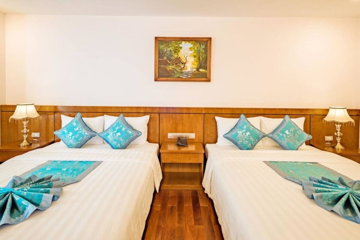 A hotel room with two beds, a nightstand, a wooden headboard, and a painting on the wall.
