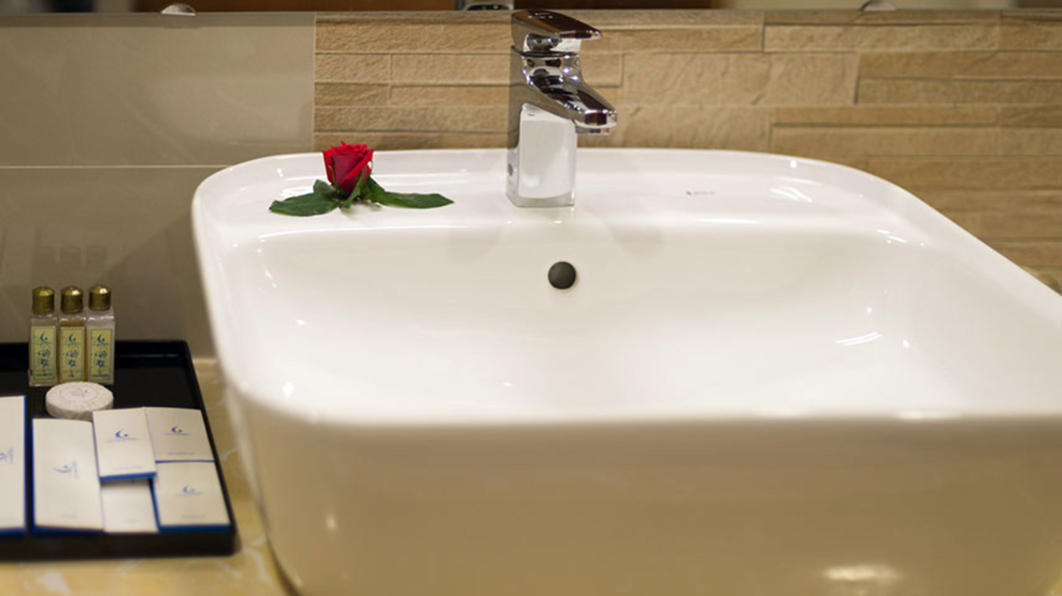 A bathroom sink with a rose, soap dispenser, and toiletries.