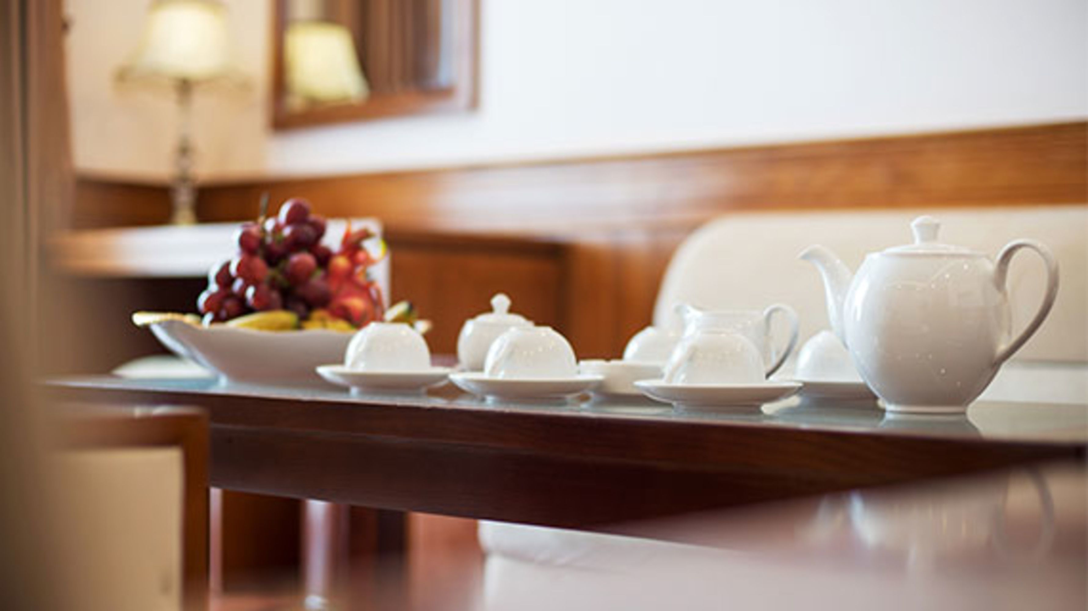 Une table avec une théière blanche, des tasses, des soucoupes et un saladier rempli de fruits.