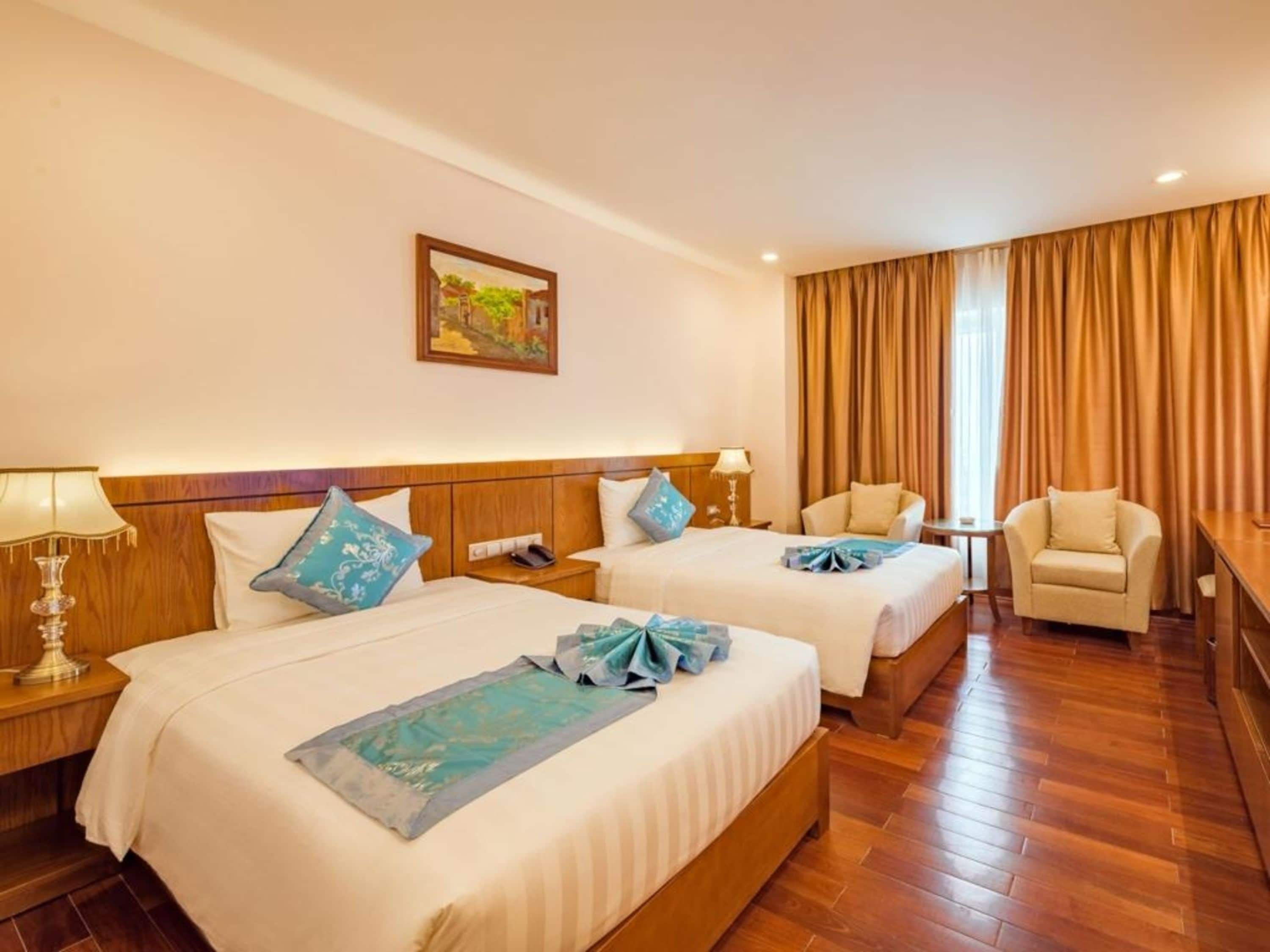 A hotel room with two beds, a desk, a chair, and a painting on the wall.
