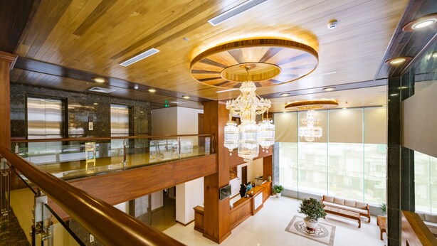 A spacious lobby with a wooden ceiling, a grand chandelier, a reception desk, and a glass railing overlooking a lower level. - Lam Giang Hotel (Thanh Vinh)