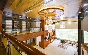 A spacious lobby with a wooden ceiling, a grand chandelier, a reception desk, and a glass railing overlooking a lower level. - Lam Giang Hotel (Thanh Vinh)