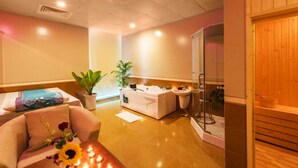 A spa room with a massage table, a sofa, a small table with candles, and a glass shower enclosure. - Lam Giang Hotel (Thanh Vinh)