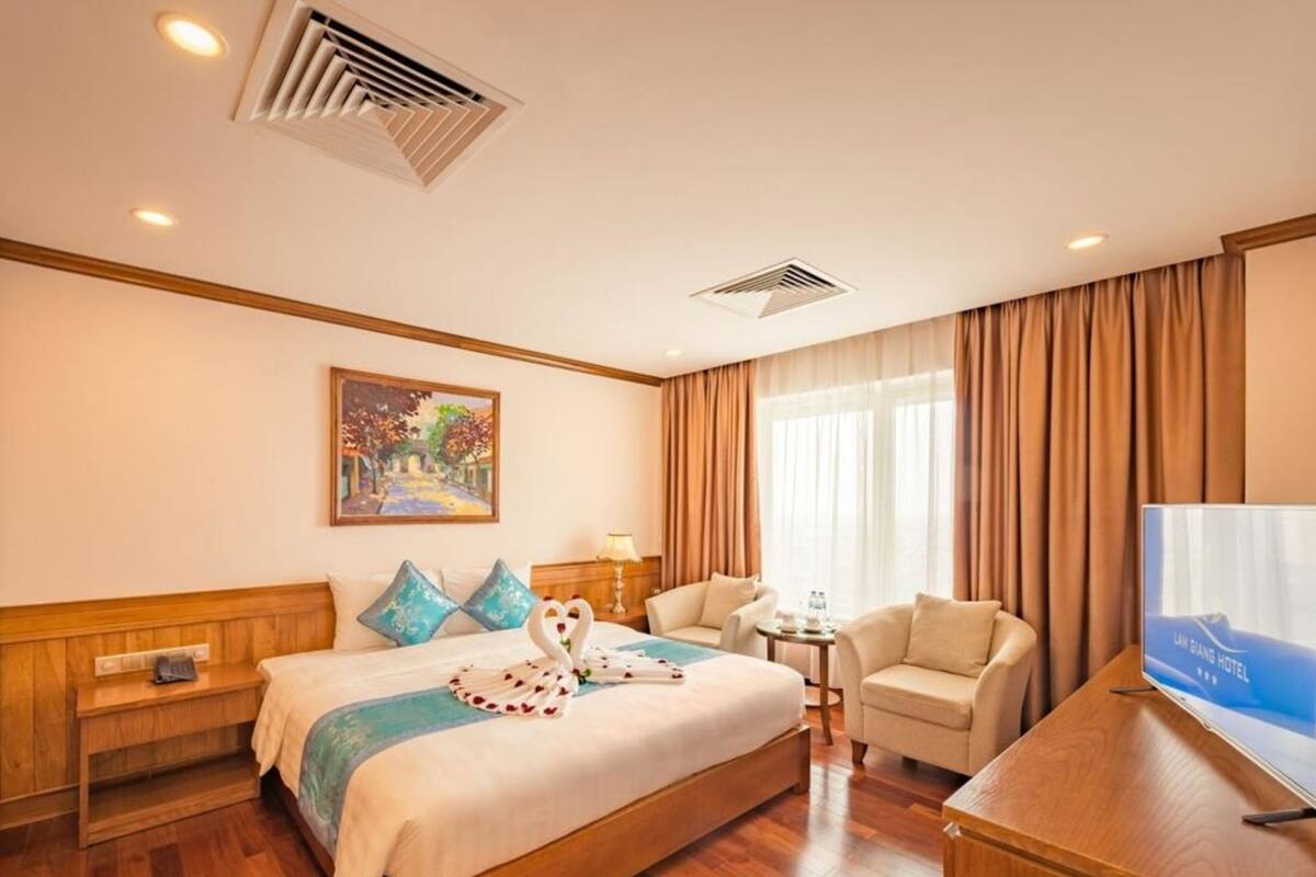 A hotel room with a bed, a desk, a chair, a TV, and a painting on the wall.
