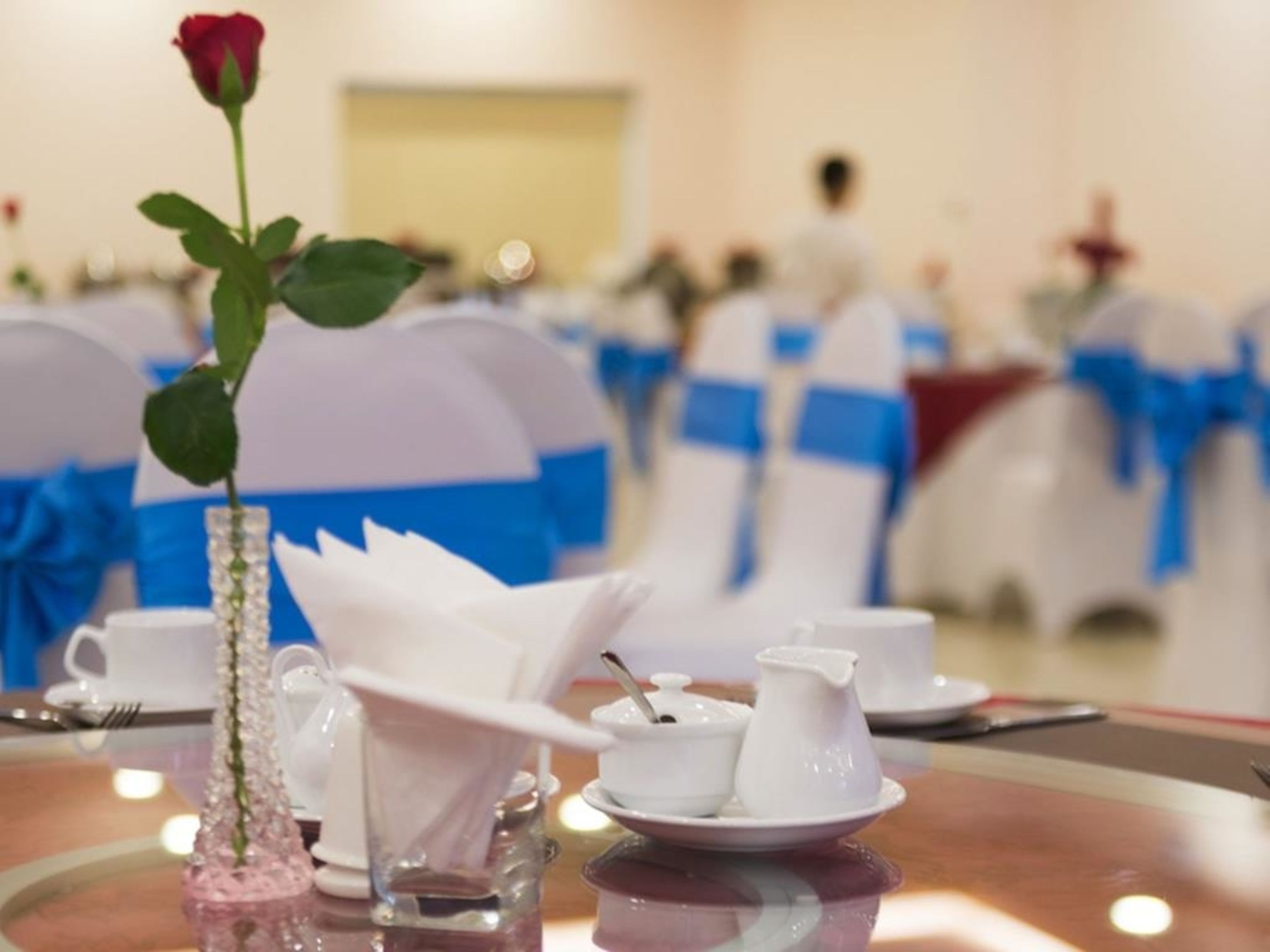 Un tavolo apparecchiato con una rosa, una brocca e una tazza, con delle sedie sullo sfondo.