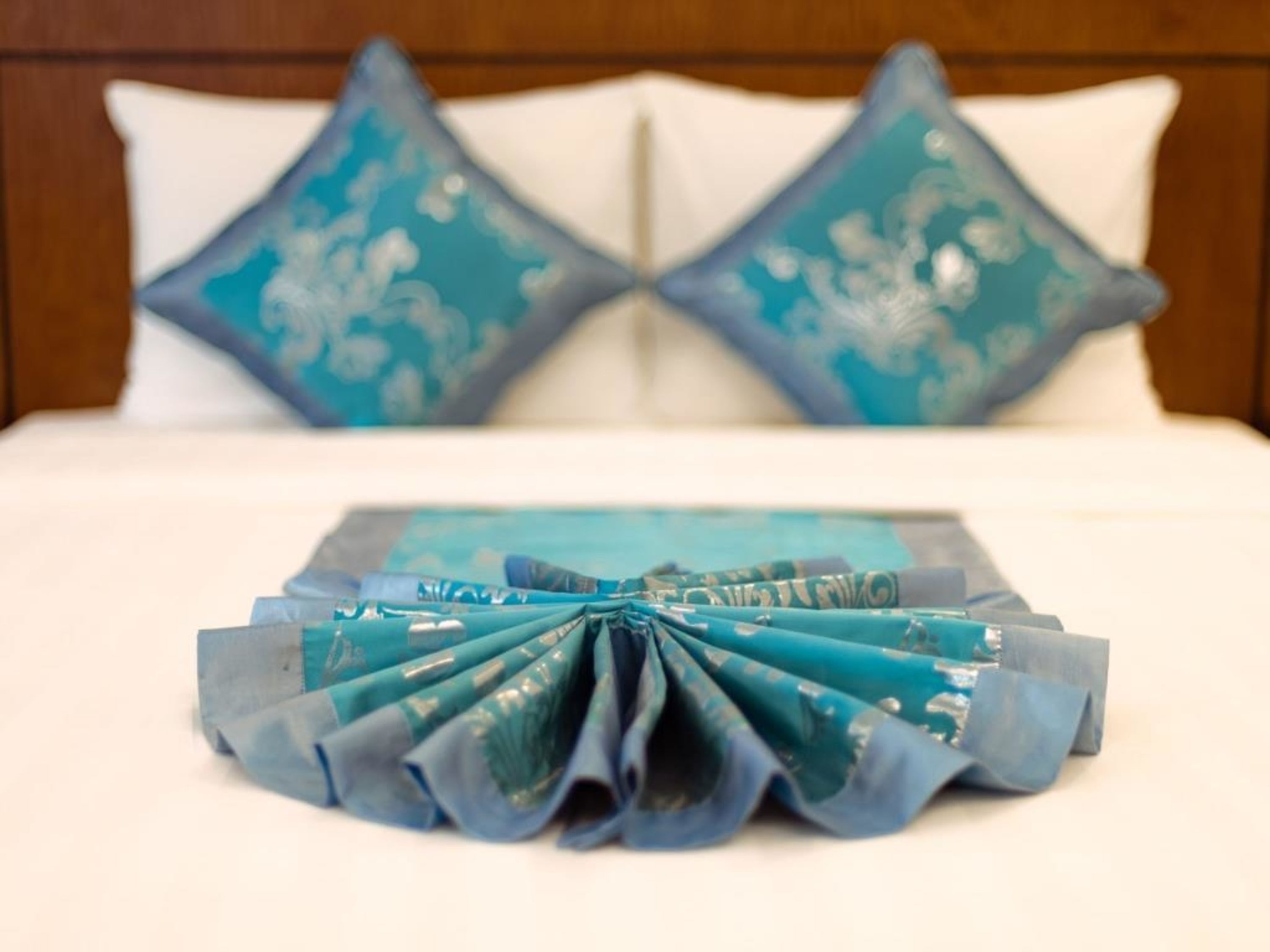 Un lit bien fait, avec du linge de lit blanc et deux coussins décoratifs ornés d’un motif floral bleu.