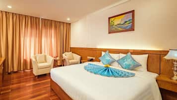 A hotel room with a large bed, two armchairs, a wooden headboard, a painting on the wall, and a curtain.
